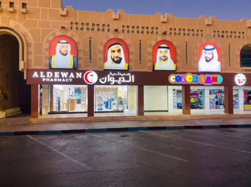 Front-lit storefront signs for Aldewan Pharmacy and Color Land under architectural arches.